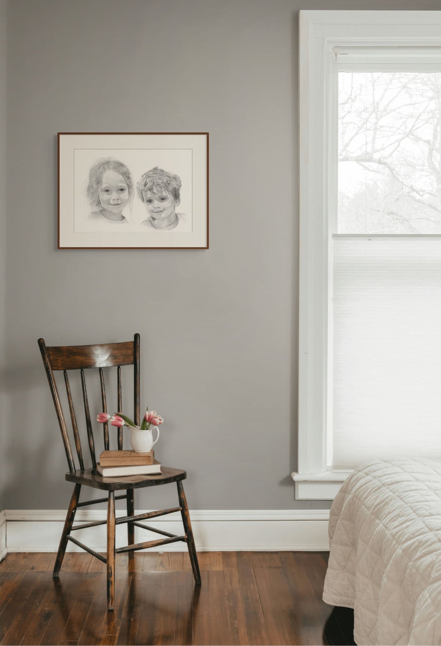 Wooden chair with a vase and books against a gray wall with a framed black and white portrait.